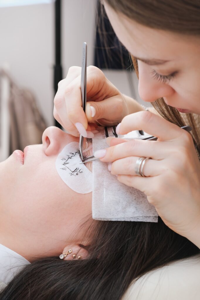 concentrated woman beautician applying eyelashes to a client face. young cosmetologist