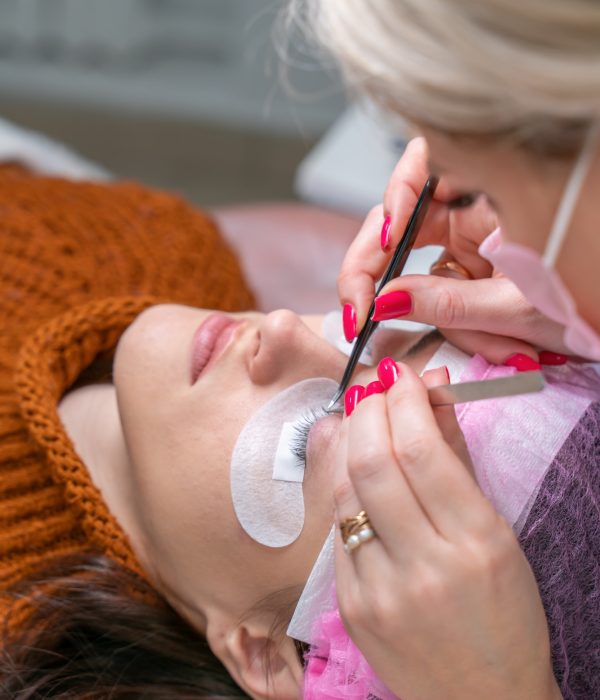 Lashmaker with tweezers glues false eyelashes to a client